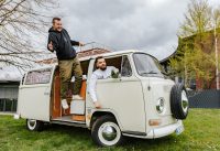 Zwei Kollegen lehnen aus einem alten VW Bus